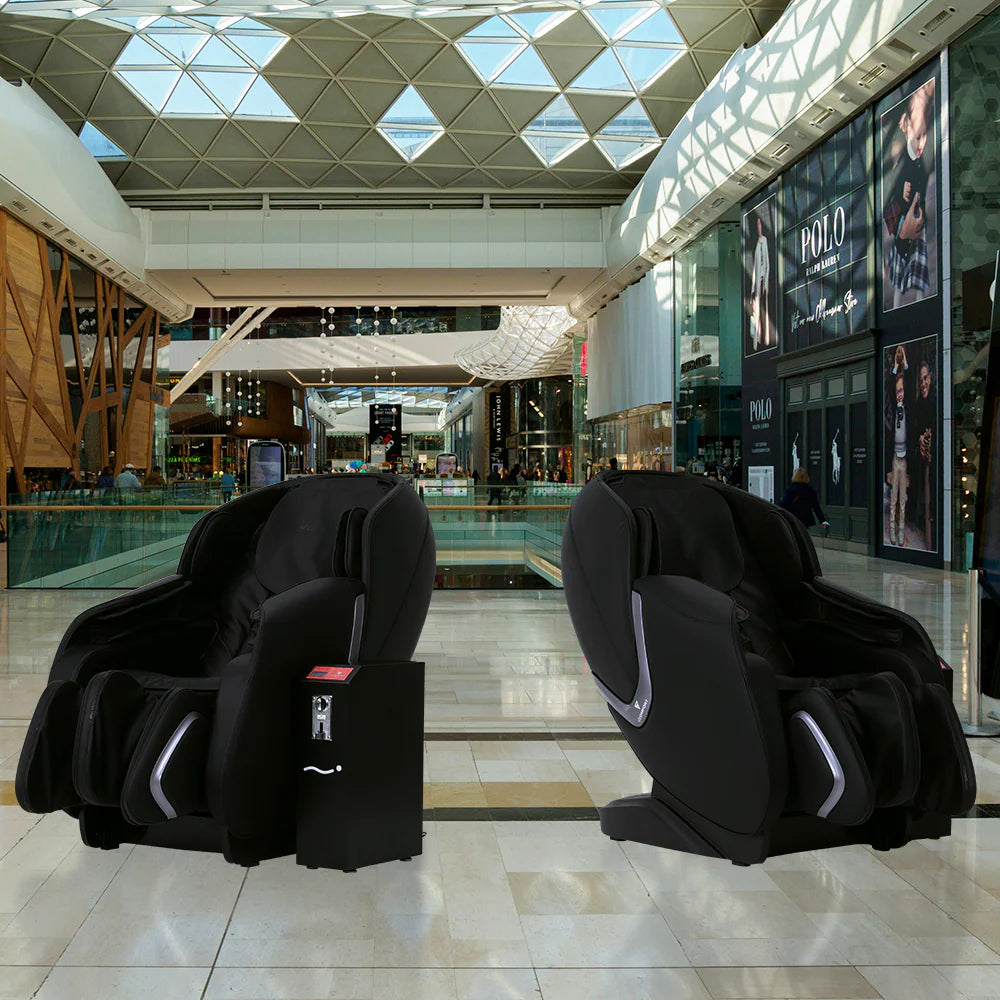 Two massage chairs in a modern mall setting with geometric ceiling design.